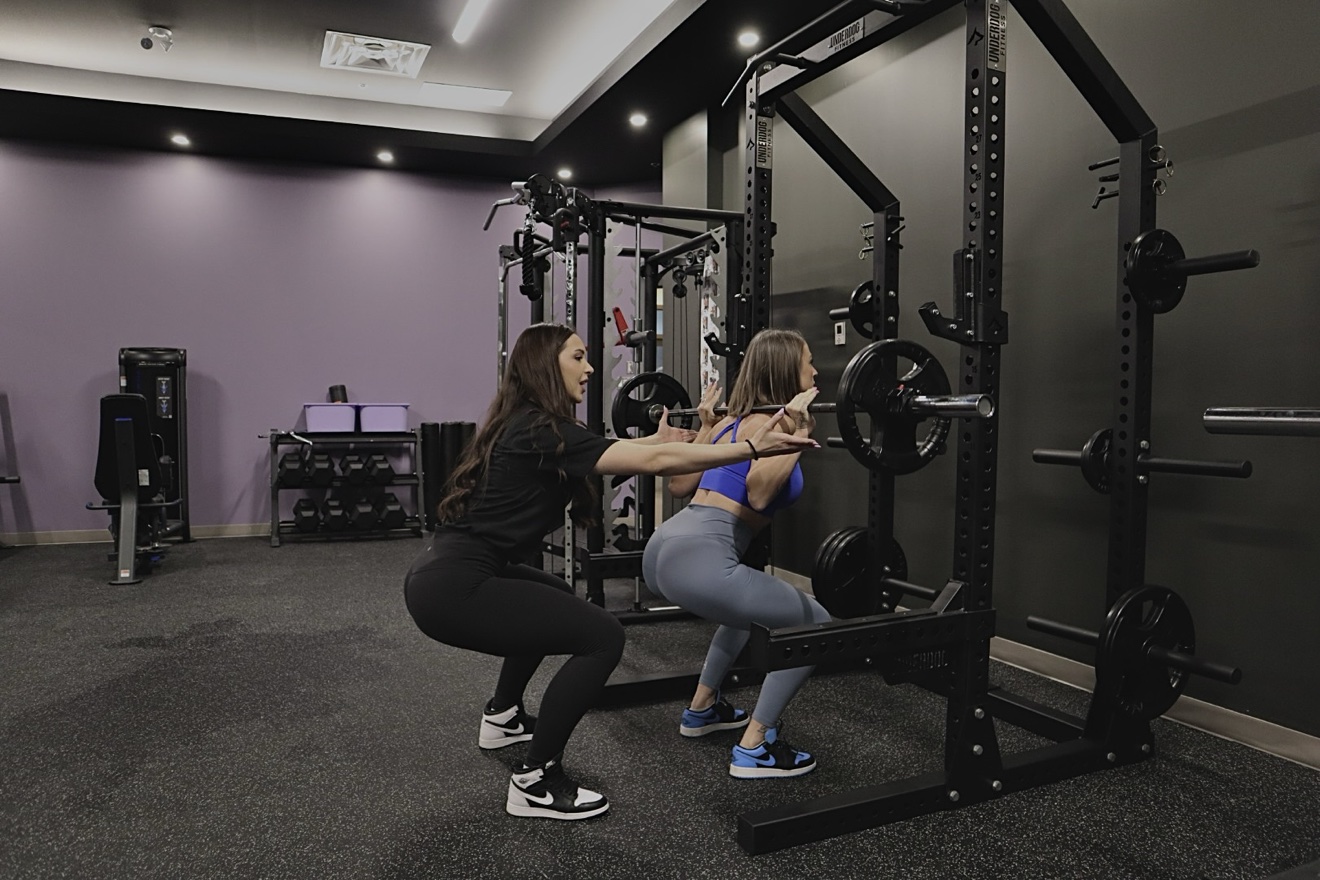 A coach guiding a client through a barbell squat in the Orléans studio